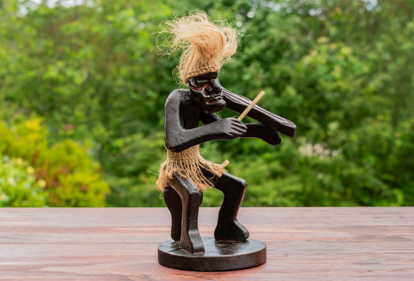 Statue of a figure playing a violin on a wooden surface with a blurred natural background