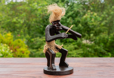 Statue of a figure playing a violin on a wooden surface with a blurred natural background