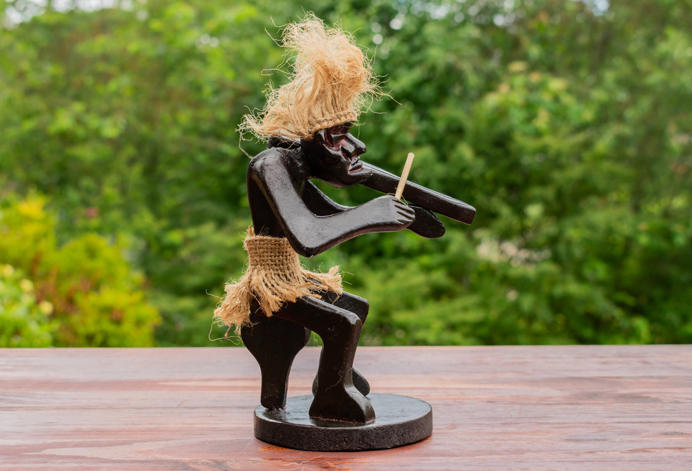 Wooden sculpture of a figure playing a flute on a wooden surface with a blurred green background