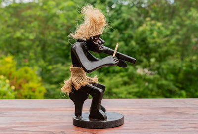 Wooden sculpture of a figure playing a flute on a wooden surface with a blurred green background