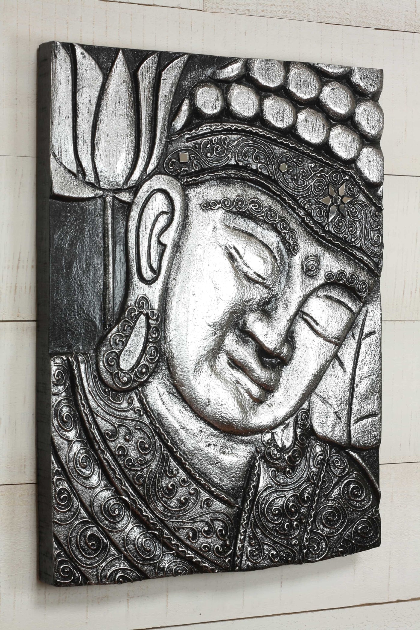 Decorative wall art of a Buddha face with intricate patterns on a light wooden background