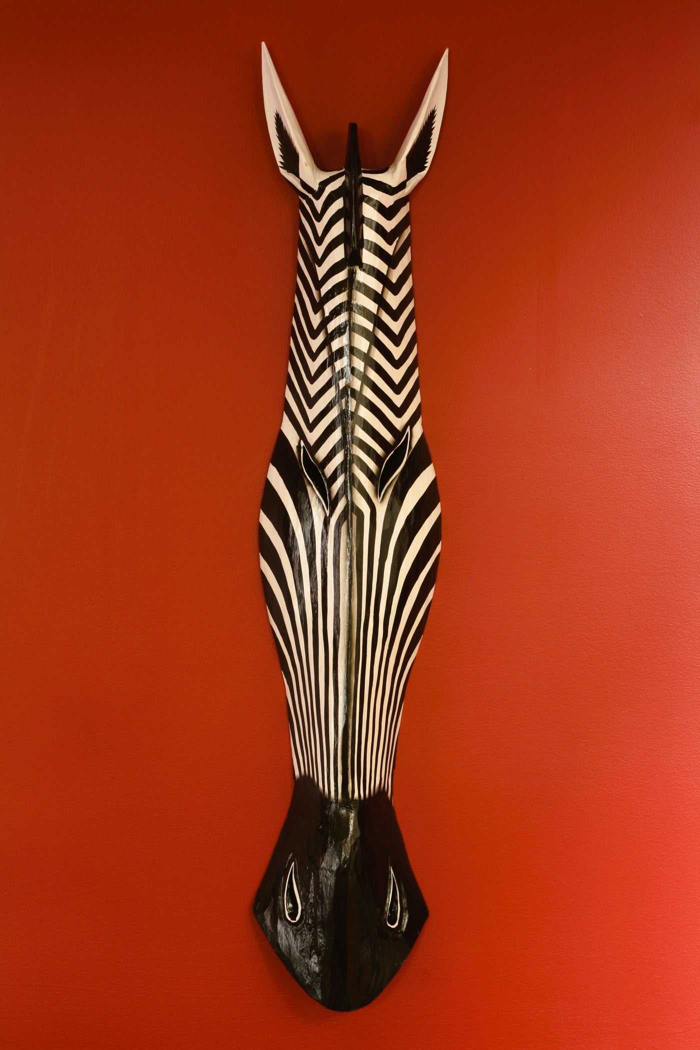 Hand carved wooden zebra head wall mask with bold black and white stripes on red wall