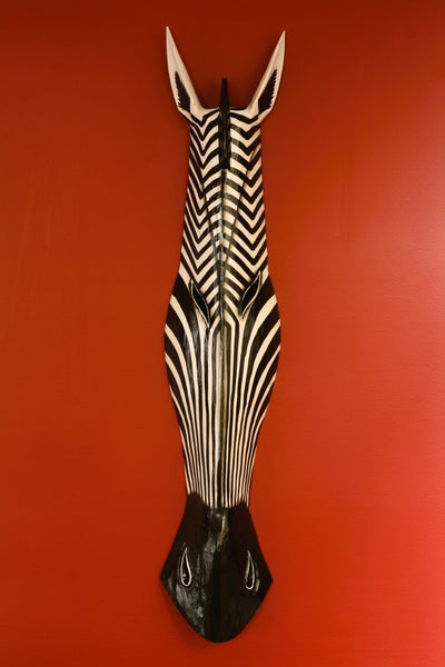 Hand carved wooden zebra head wall mask with bold black and white stripes on red wall
